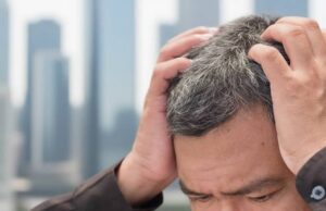 Мужчина держится за голову, испытывая стресс — фактор ранней седины