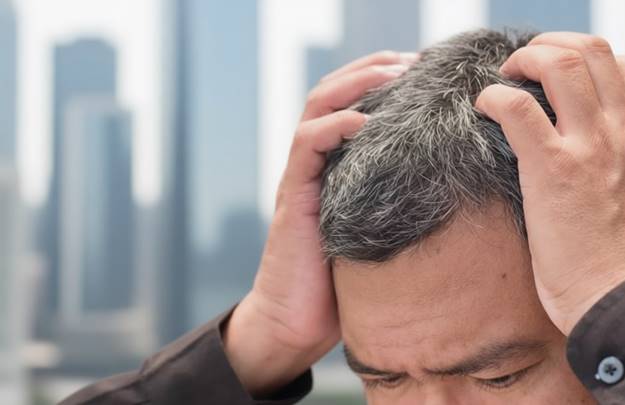 Мужчина держится за голову, испытывая стресс — фактор ранней седины