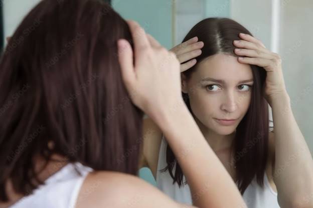 Подросток, разглядывающий свои волосы в зеркале, отражающее беспокойство о жирности или выпадении