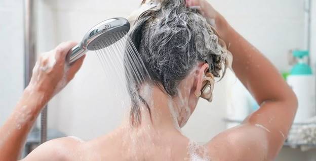 Женщина наносит шампунь на волосы