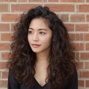 Девушка с естественными мягкими волнистыми волосами, позирующая у стены