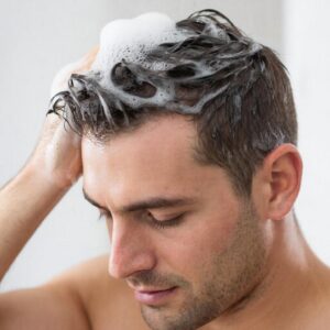 Мужчина моет голову шампунем, вспенивая волосы вручную