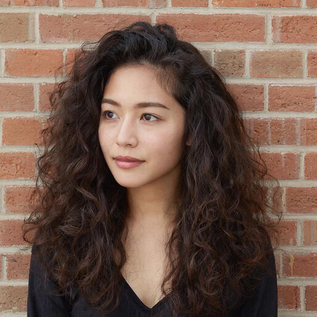 Девушка с естественными мягкими волнистыми волосами, позирующая у стены