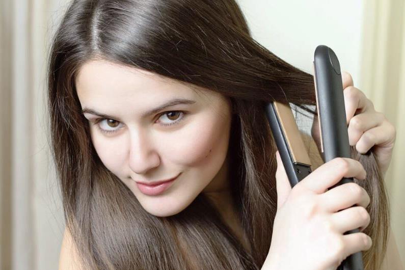 Девушка выпрямляет волосы утюжком