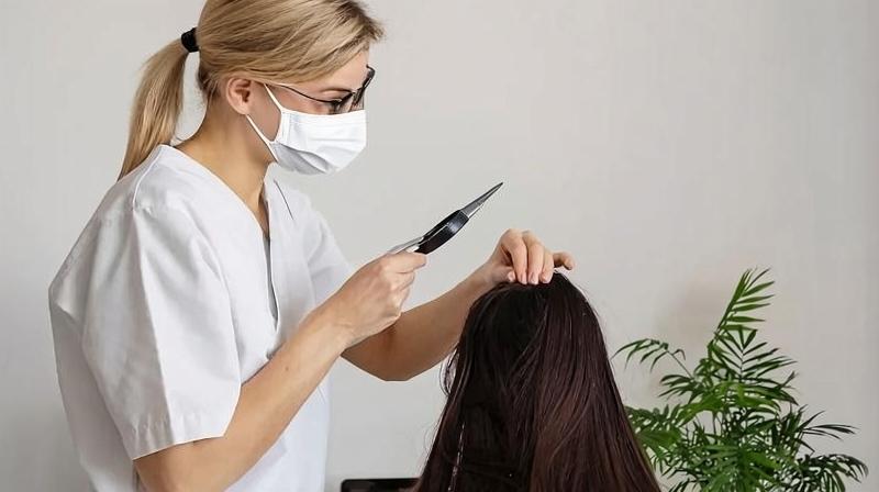 Трихолог проводит обследование кожи головы пациентки с помощью дерматоскопа