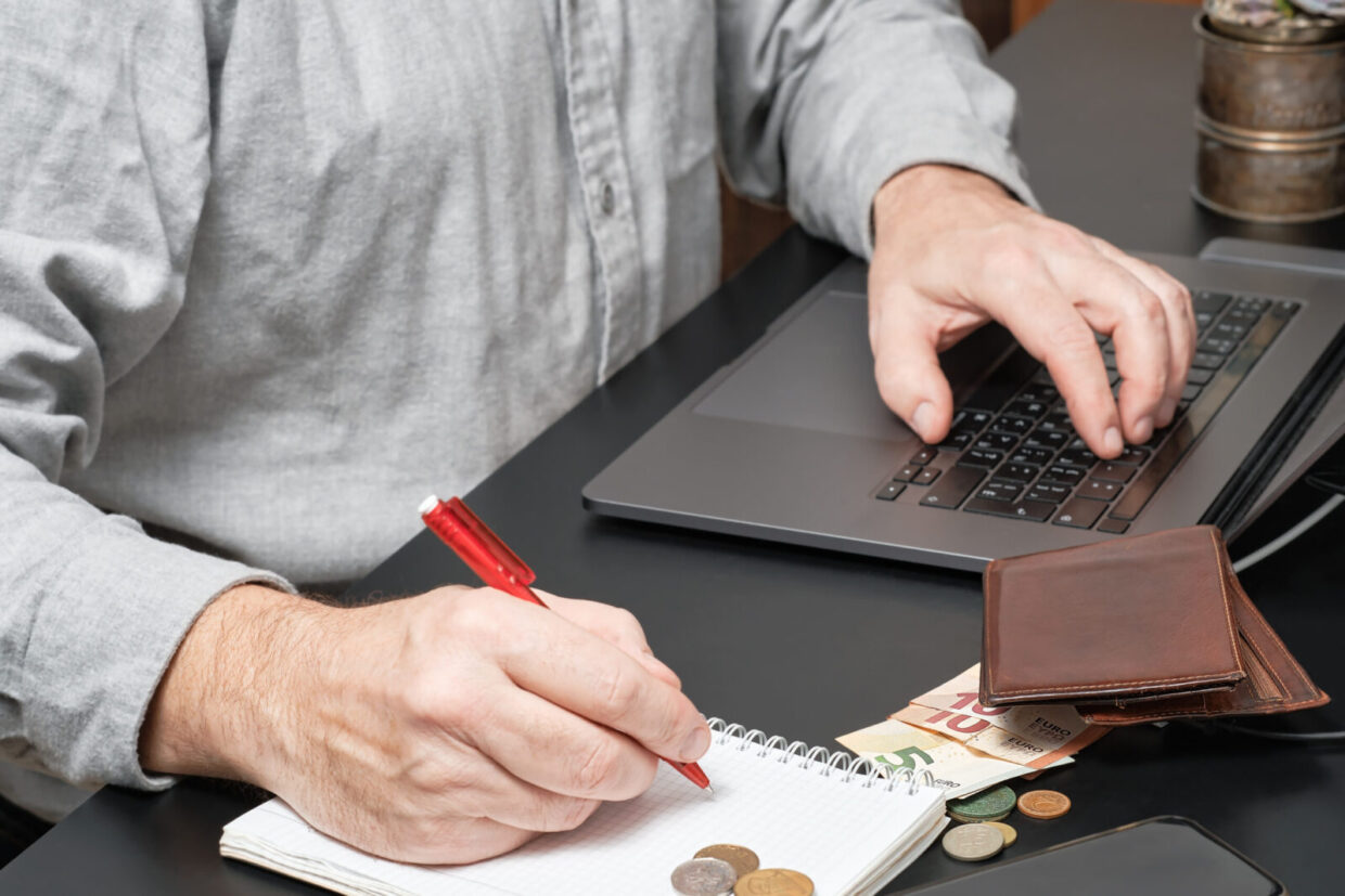 close up of a businessman or accountant holding pen working at desk using a laptop to calculate financial report or tax payments. business concept of accounting, paying taxes, calculating finances