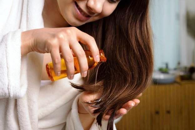 Девушка наносит масло на кончики волос для ухода после антибиотиков