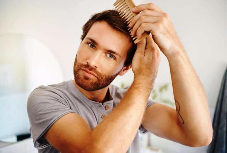 Мужчина расчесывает волосы деревянной расческой