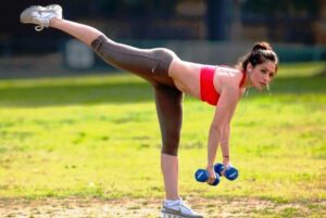 Девушка выполняет упражнение с гантелями на свежем воздухе