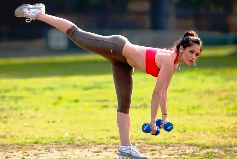 Девушка выполняет упражнение с гантелями на свежем воздухе