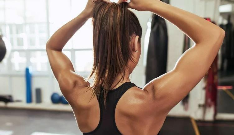 Девушка собирает волосы в хвост в спортзале